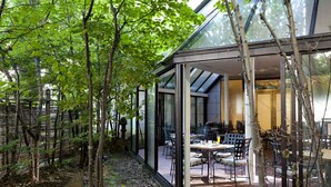 Une terrasse vitrée avec des sièges extérieurs, entourée d’arbres.