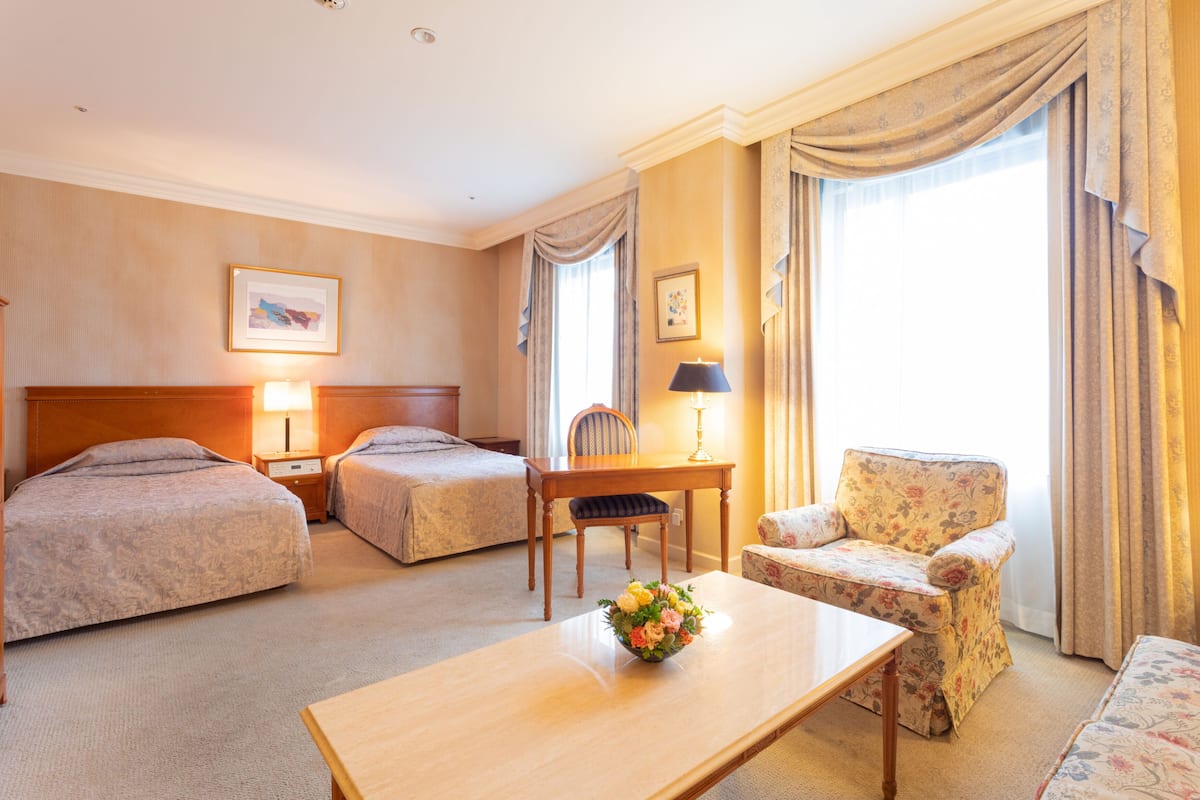 A hotel room with two beds, a wooden table with a vase of flowers, a chair, and a desk.