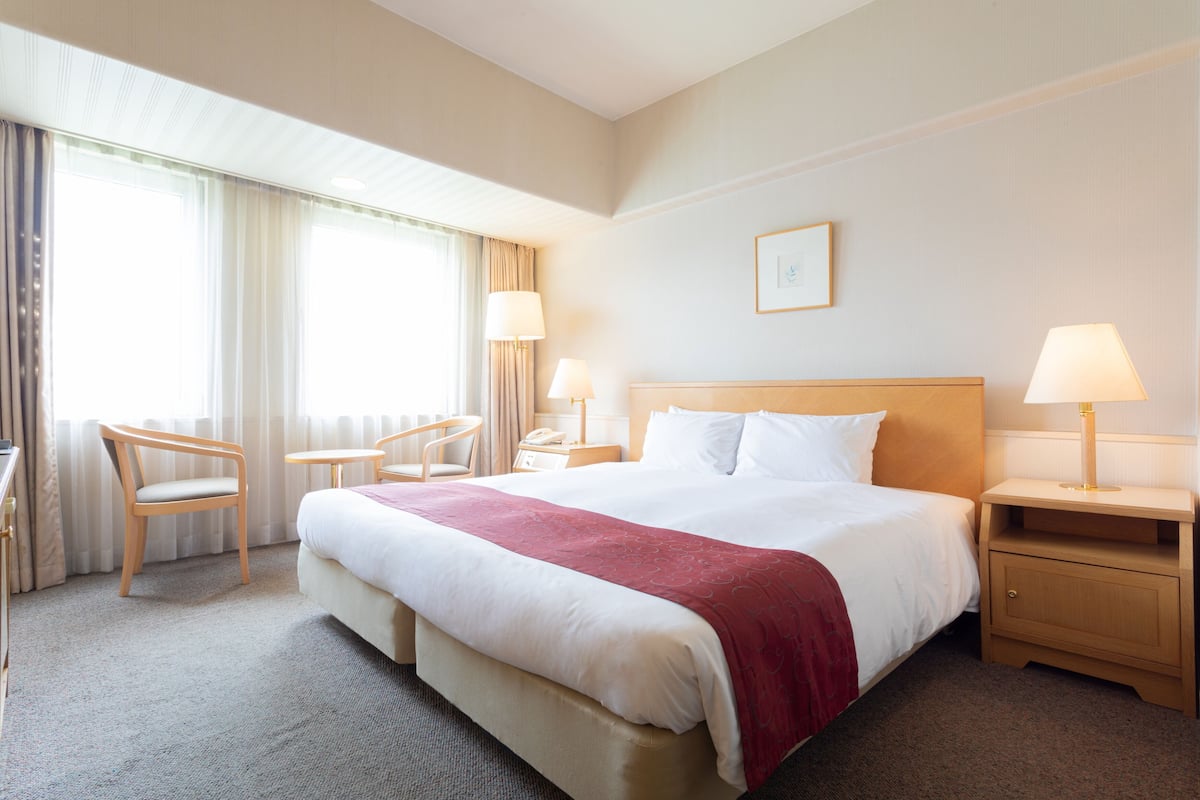 A hotel room with a large bed, two bedside tables with lamps, a chair, and a desk.