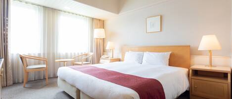 A hotel room with a large bed, two bedside tables with lamps, a chair, and a desk.