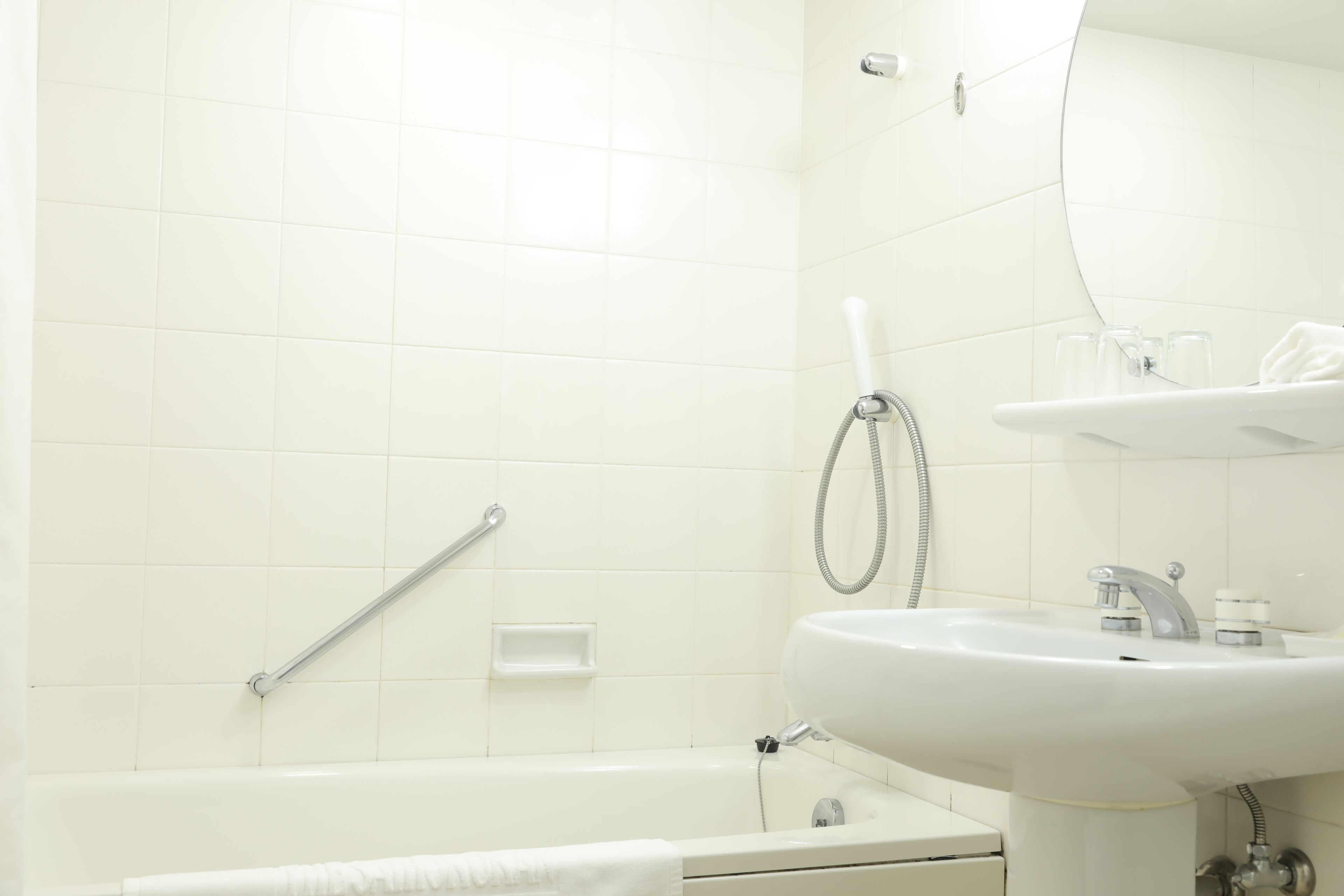 Een badkamer met een witte badkuip, een wastafel met een spiegel erboven en een douchekop.