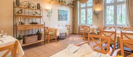 A dining area with multiple tables set for guests, wooden chairs, and a wine rack with bottles.