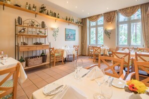 A dining area with multiple tables set for guests, wooden chairs, and a wine rack with bottles. - Best Western Hotel Geheimer Rat (Magdeburg)