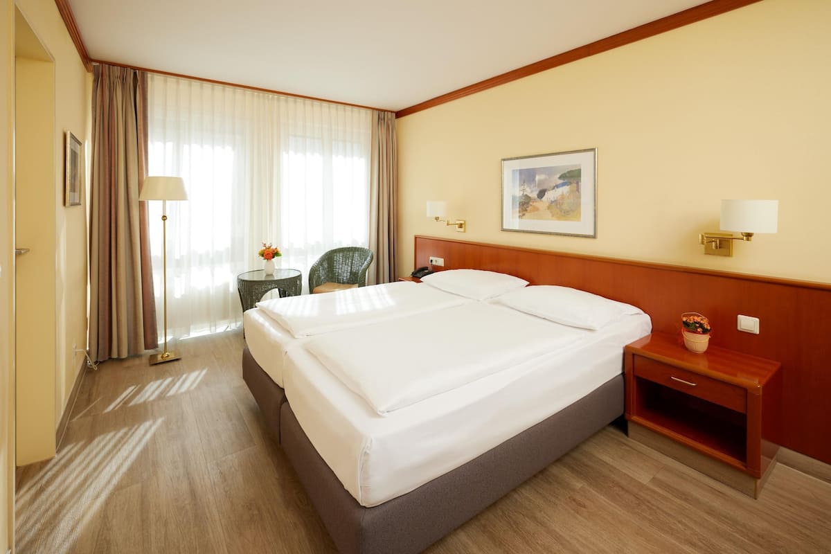 A hotel room with a large bed, a bedside table with a lamp, a chair, and a painting on the wall.