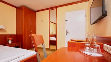 A hotel room with a bed, a desk, a chair, a wardrobe, a television, and a mirror.
