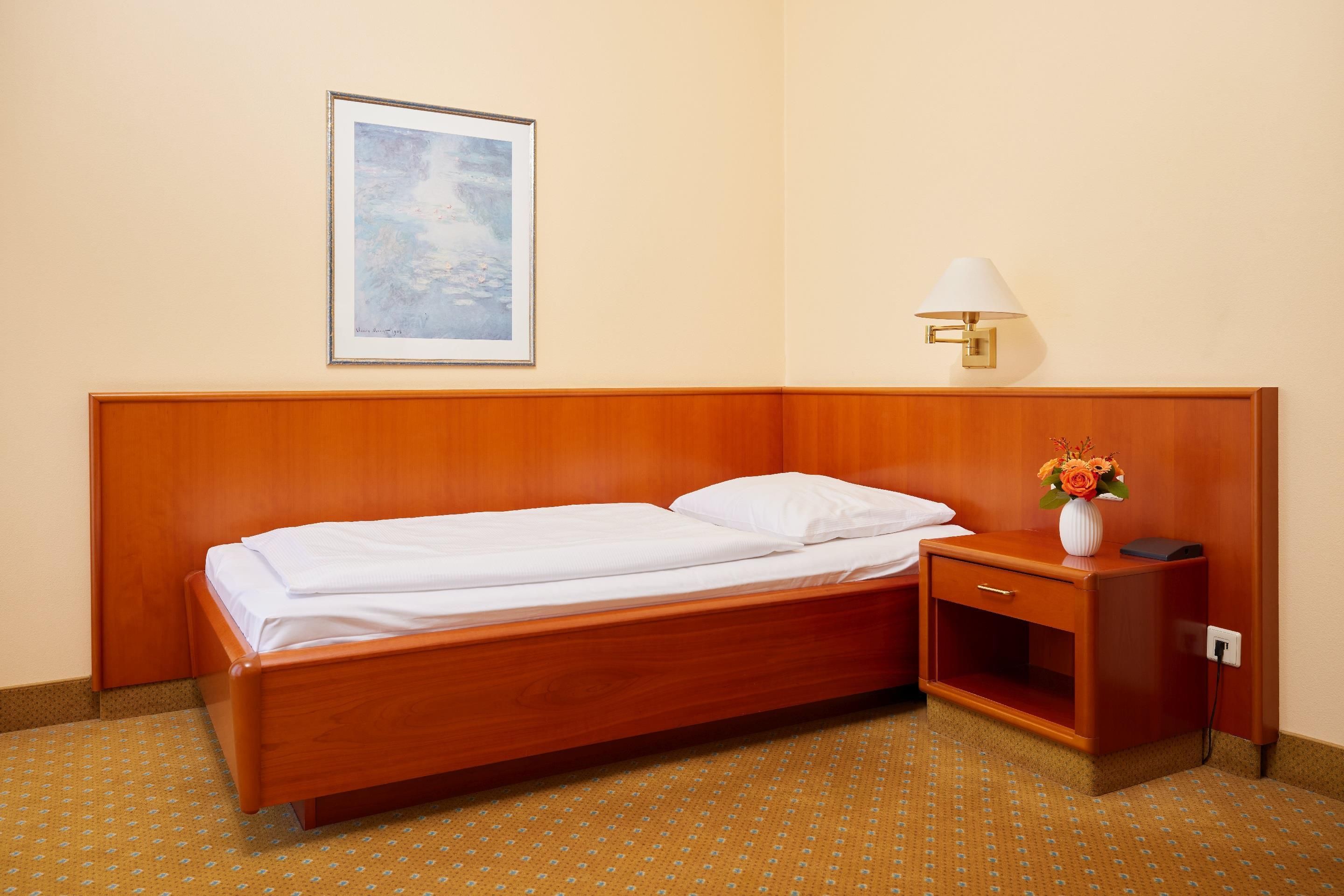 A hotel room with a single bed, a nightstand, a lamp, and a framed picture on the wall.
