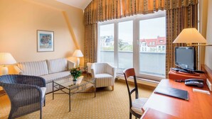 A hotel room with a sofa, armchairs, a desk with a TV, and a window with a view of buildings. - Best Western Hotel Geheimer Rat (Magdeburg)