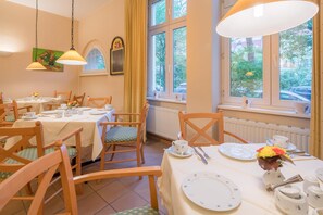 A dining area with multiple tables set for tea service, wooden chairs, and a view of greenery through large windows. - Best Western Hotel Geheimer Rat (Magdeburg)
