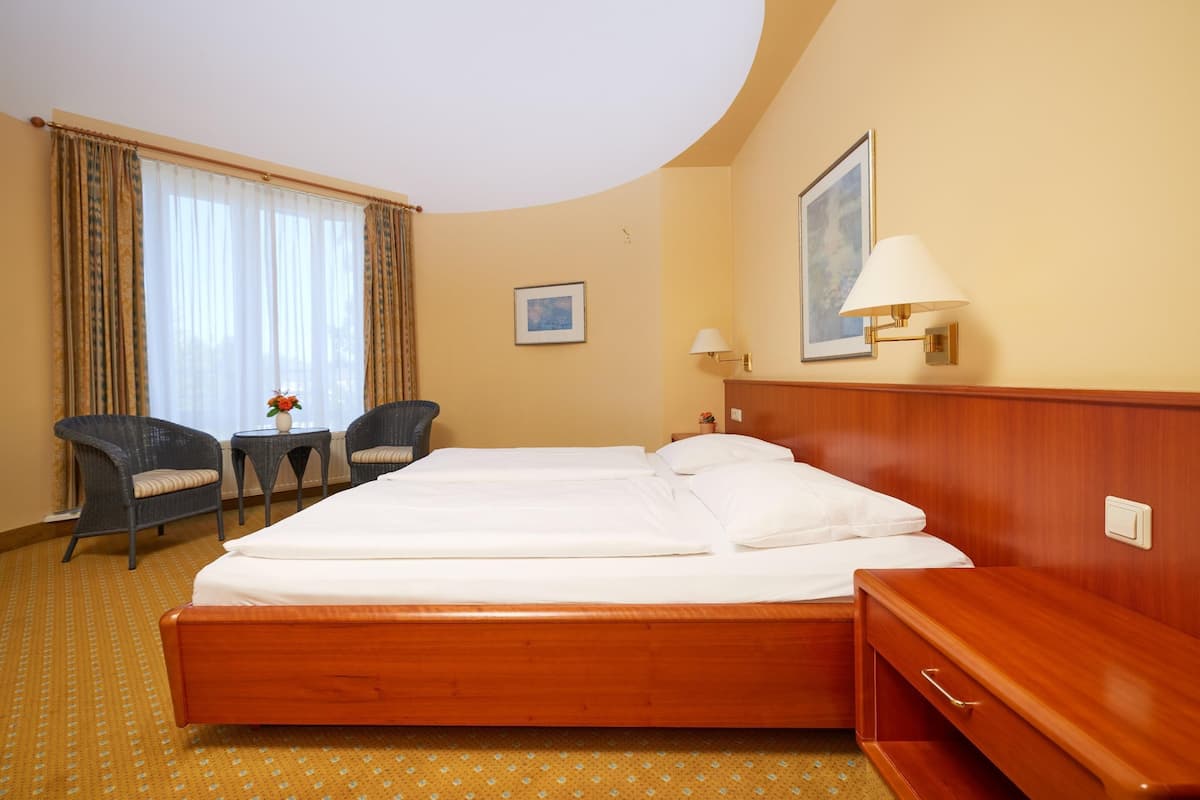 A hotel room with a large bed, two chairs, a small table with a vase, and a lamp.