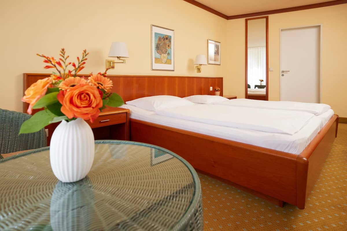 A hotel room with a wooden bed, a glass table with a white vase, and two wall-mounted lamps.