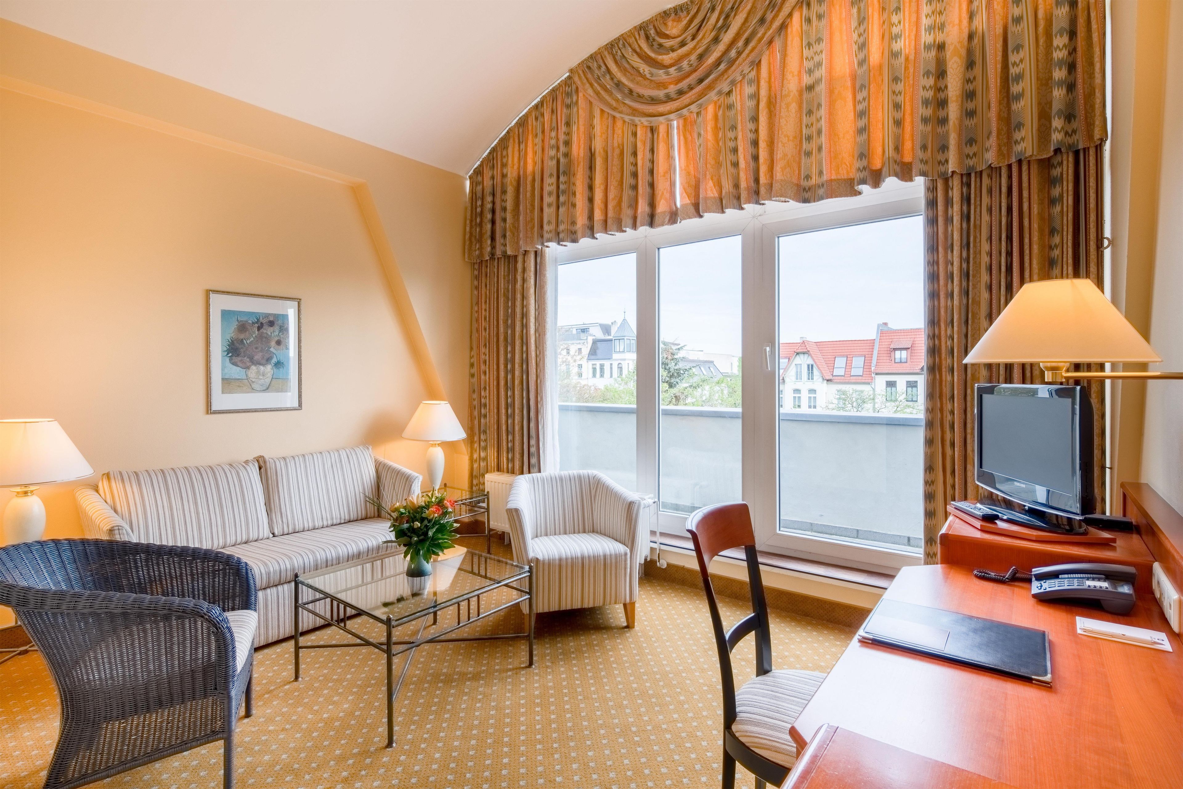 Habitación de hotel con sofá, sillones, mesa de centro, televisor y escritorio con lámpara.