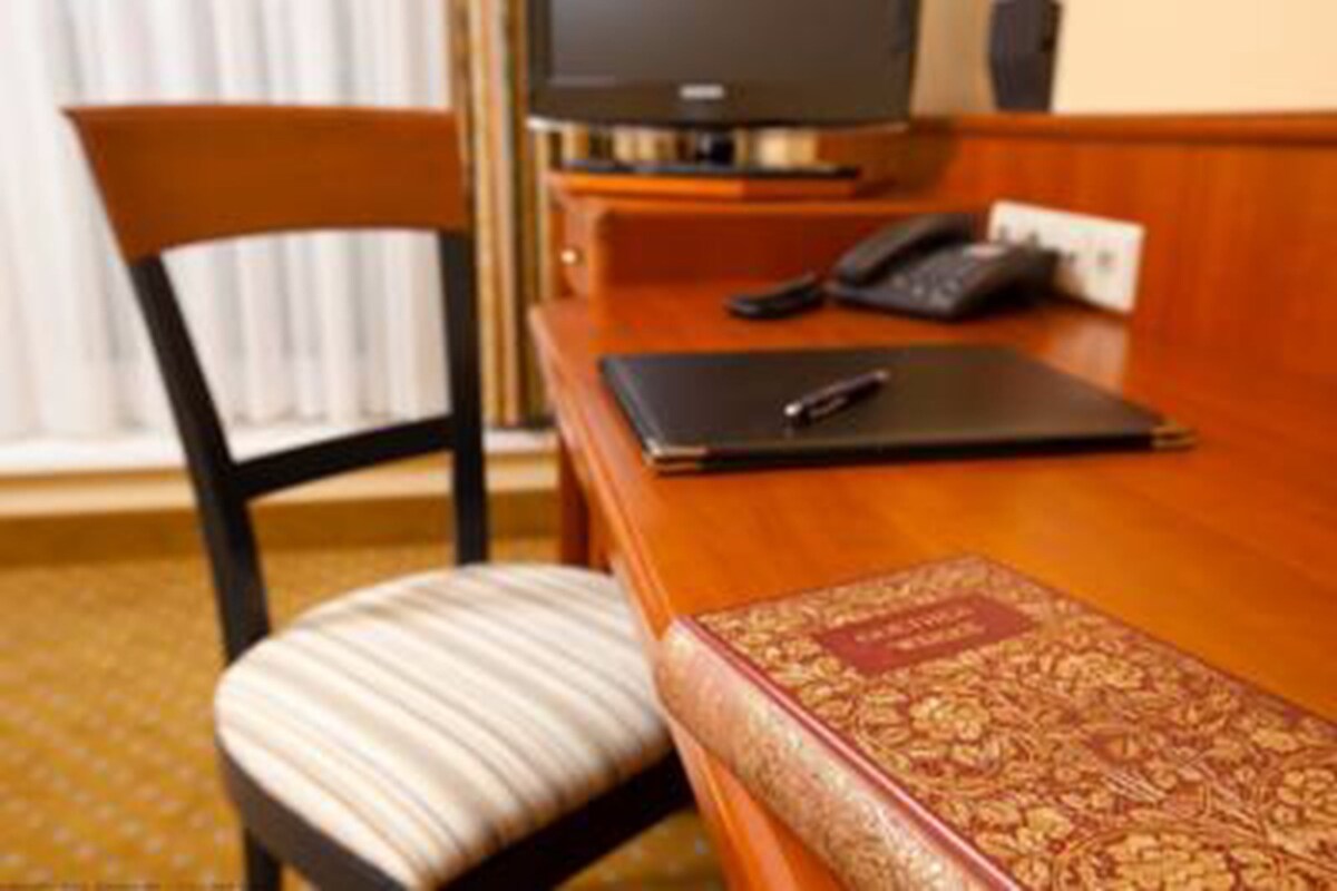 A hotel room with a wooden desk, a chair, a telephone, and a book.