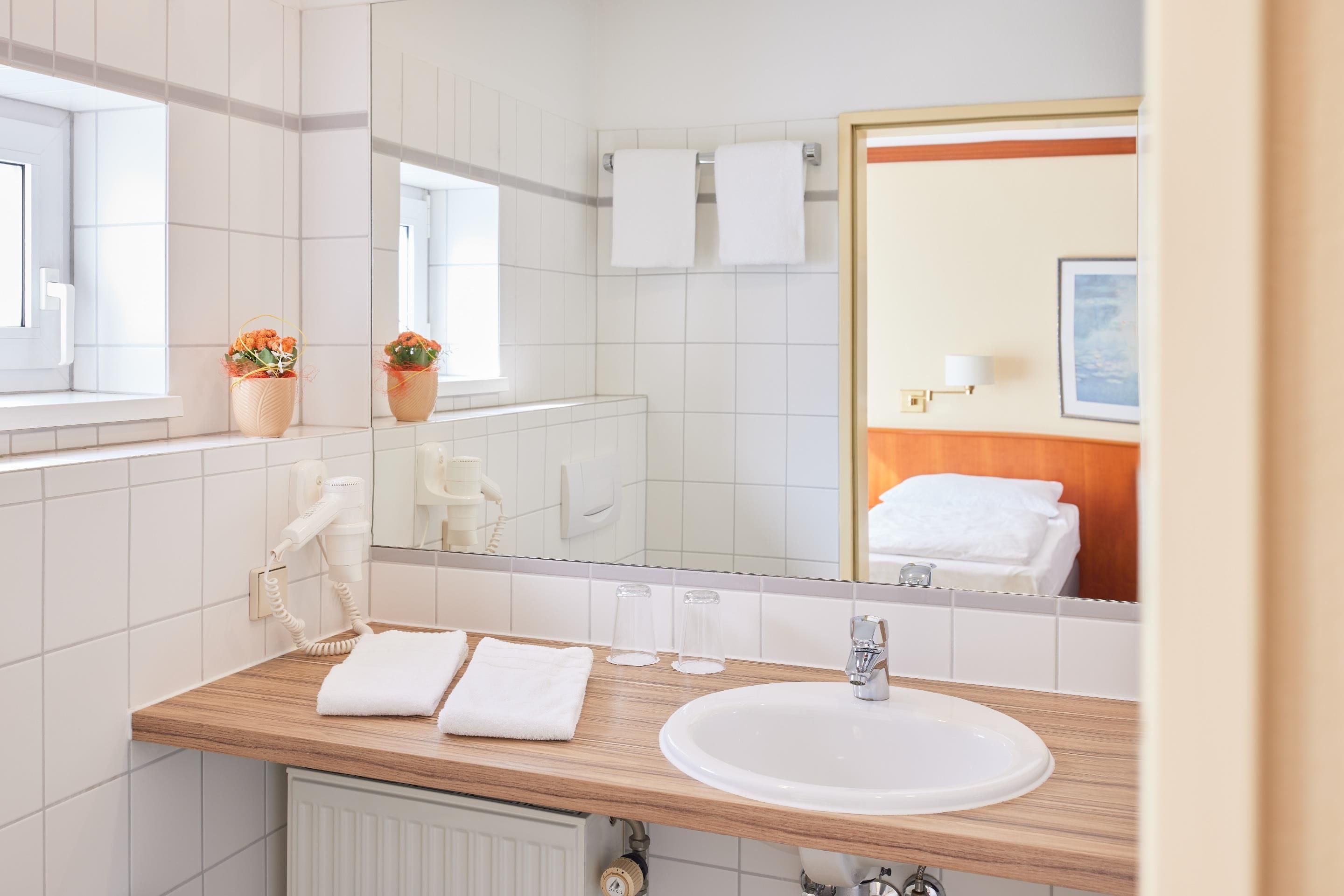 A hotel bathroom with a sink, mirror, towel rack, and a window with a view.