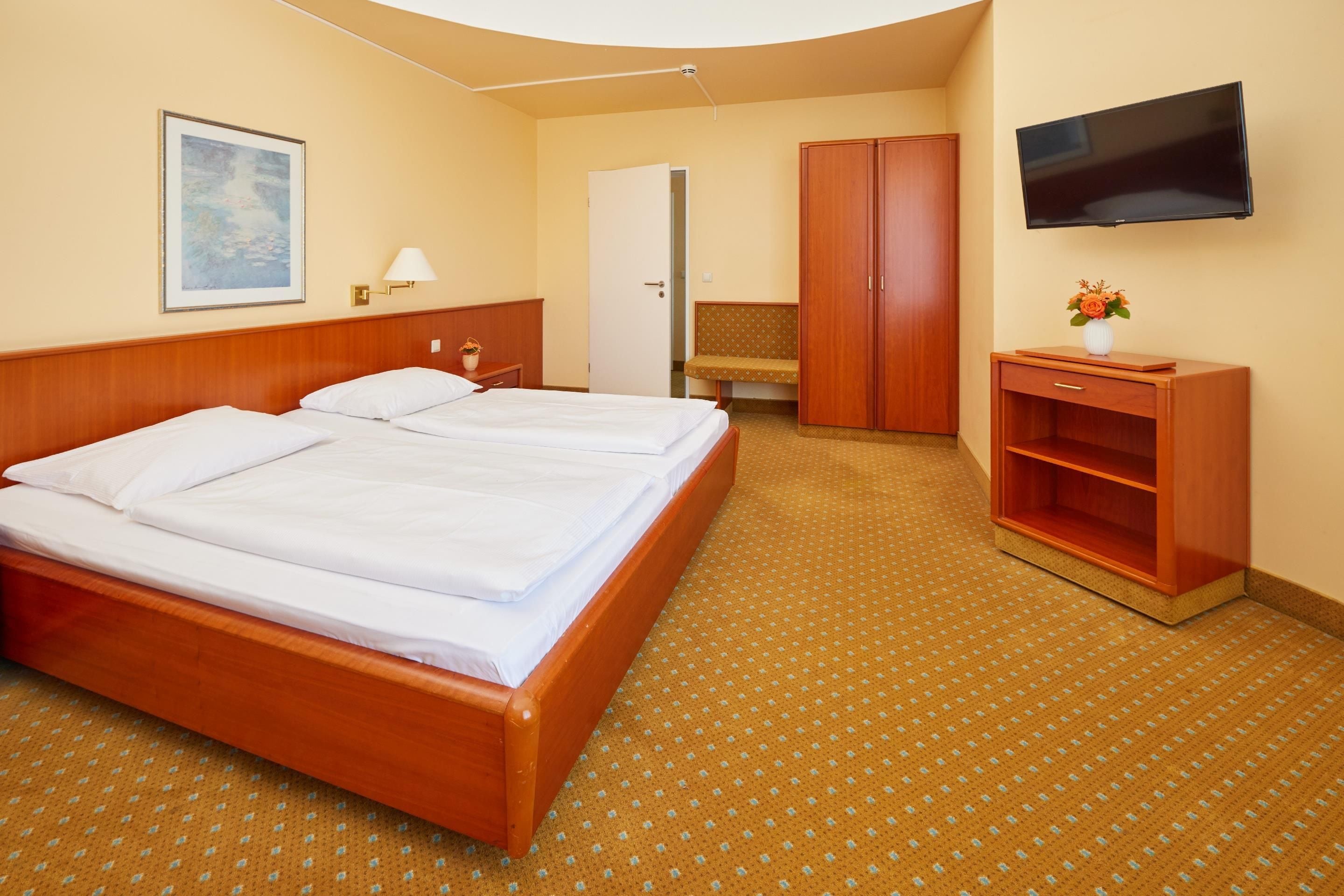 Ein Hotelzimmer mit Doppelbett, Fernseher, Kleiderschrank und einer Bank.