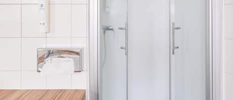 A bathroom with a glass-enclosed shower, a round mirror, and a white sink.