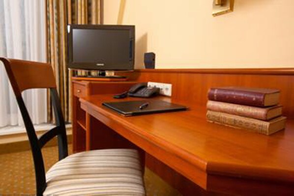 A hotel room with a wooden desk, a television, a telephone, and a stack of books. - Best Western Hotel Geheimer Rat (Magdeburg)