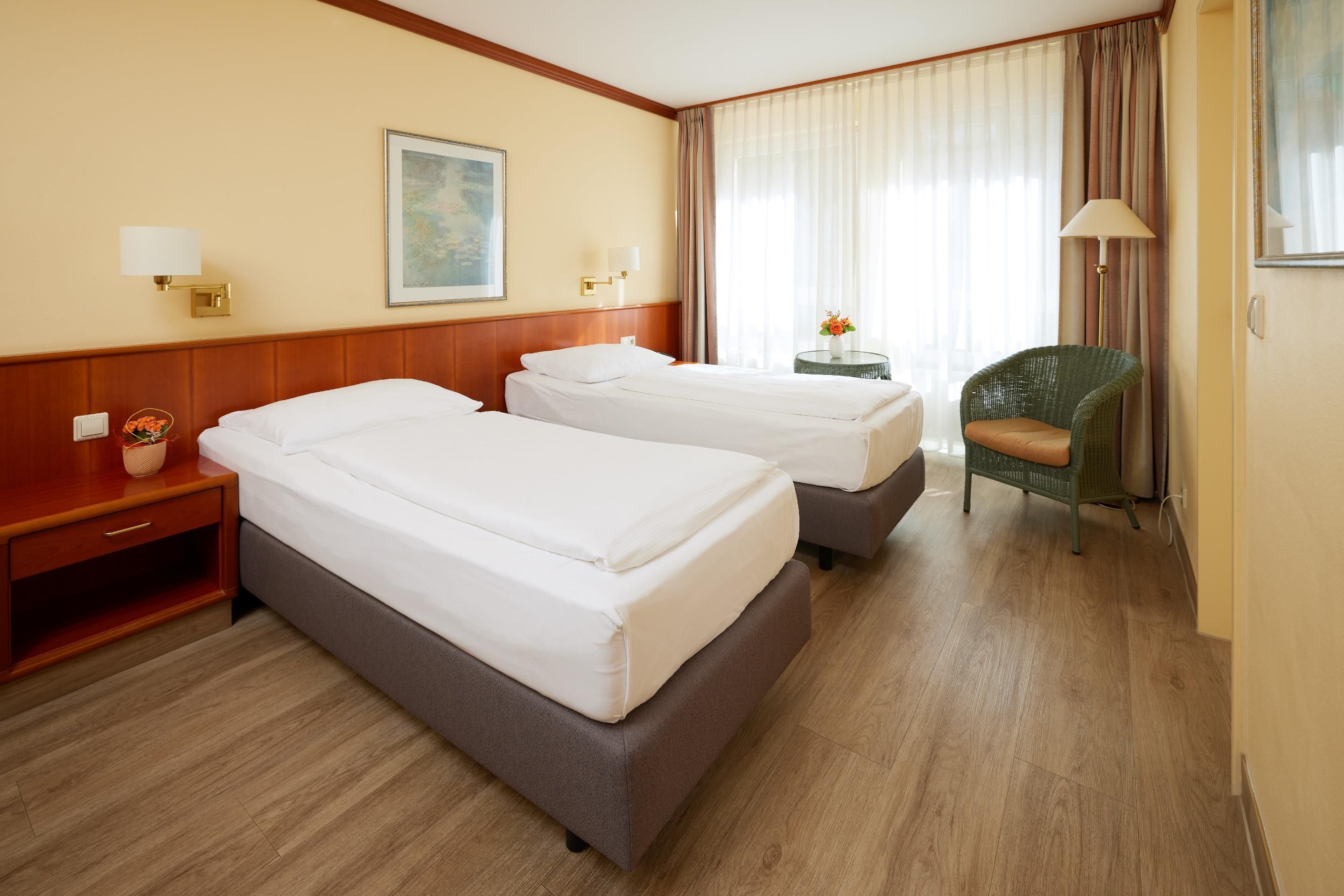 Habitación de hotel con dos camas, una mesita de noche, una silla, una lámpara y un cuadro en la pared.