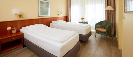 Habitación de hotel con dos camas, una mesita de noche, una silla, una lámpara y un cuadro en la pared.