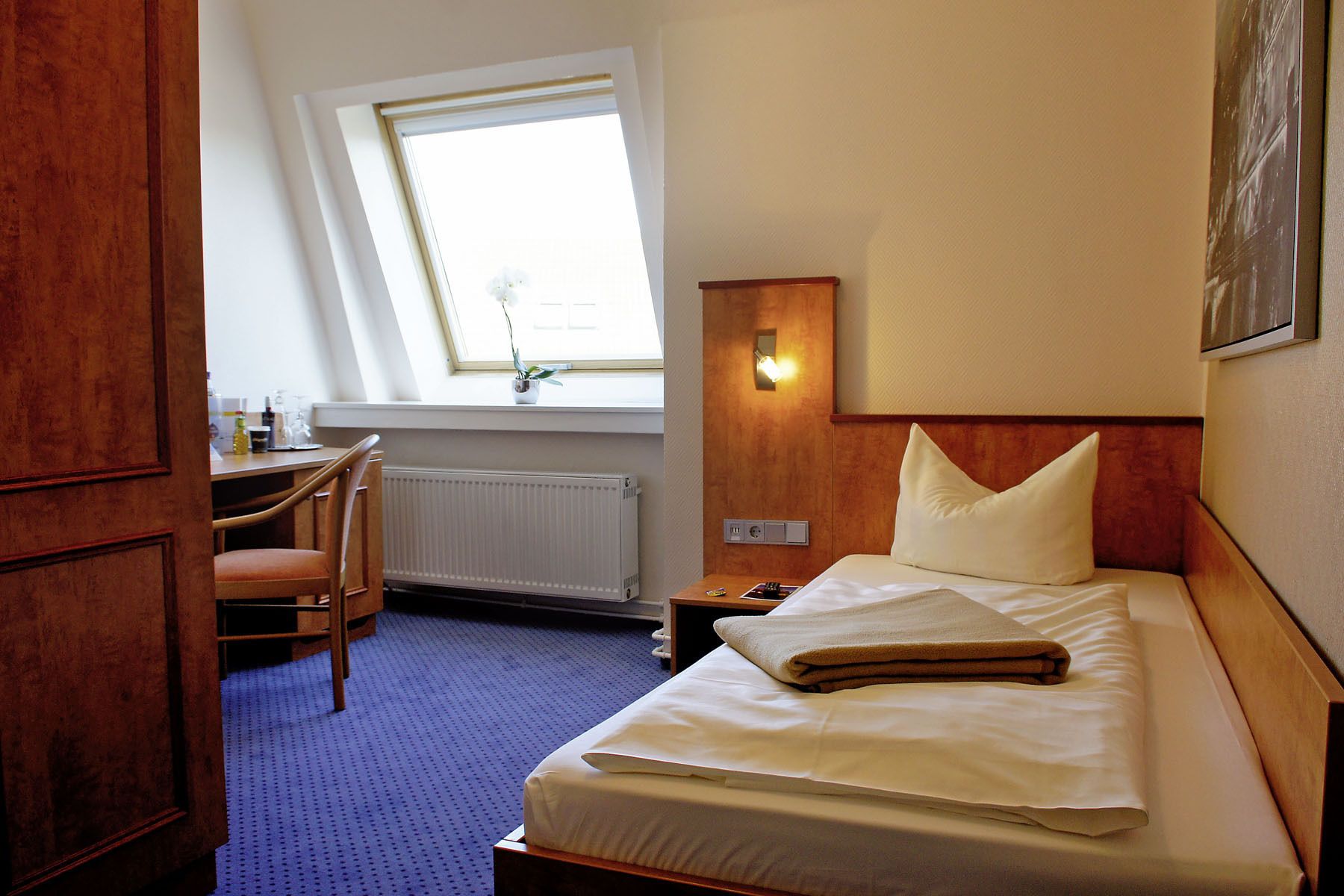 Een hotelkamer met een bed, een bureau, een stoel, een raam en een wandlamp.
