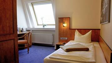 Een hotelkamer met een bed, een bureau, een stoel, een raam en een wandlamp.
