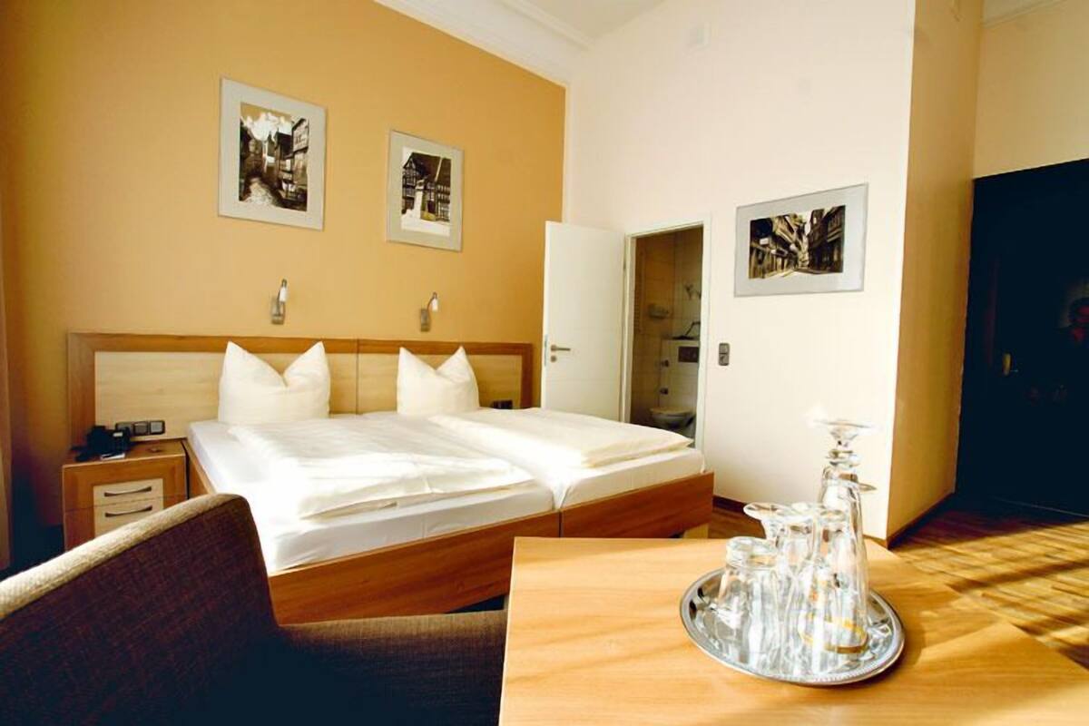 A hotel room with a large bed, a bedside table, a chair, and a tray with glassware.