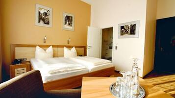 A hotel room with a large bed, a bedside table, a chair, and a tray with glassware.