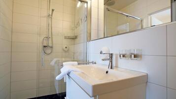 A modern bathroom with a glass-enclosed shower, a white sink, and a large mirror.