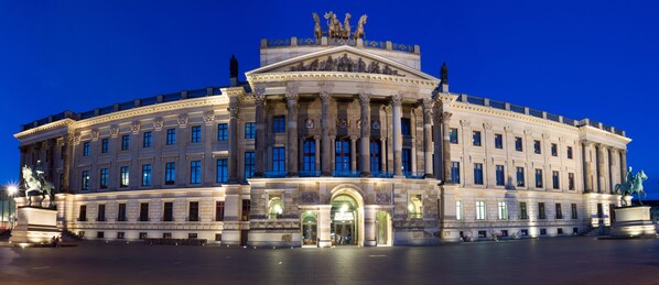 Un edificio majestuoso de estilo clásico con una entrada central, grandes columnas y estatuas en la fachada.