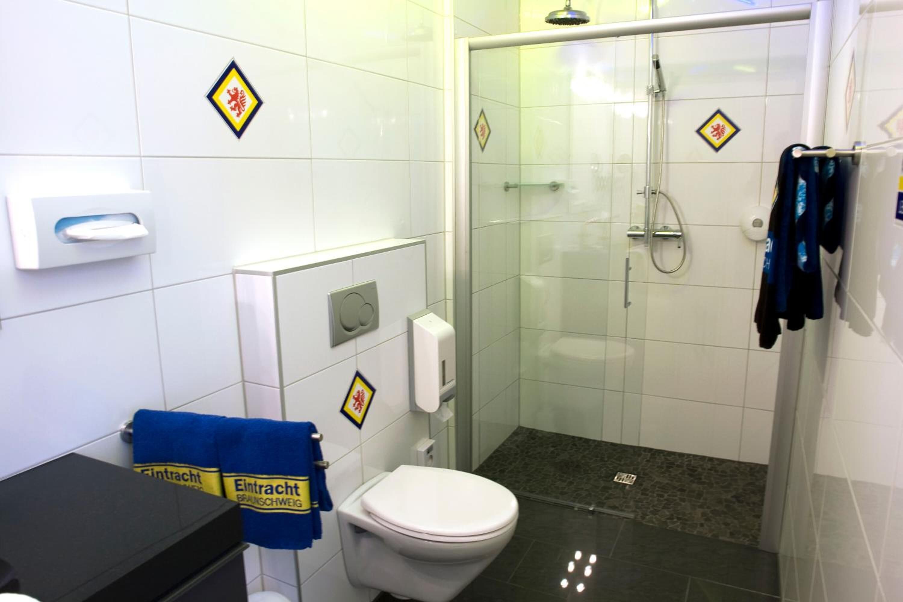 Ein Badezimmer mit Toilette, Handtrockner, einer Duschkabine und einem Handtuchhalter mit Handtüchern.