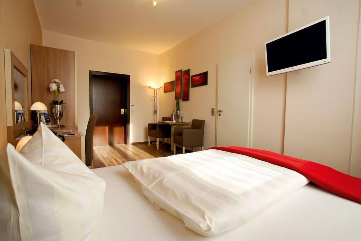 A hotel room with a bed, a desk, a chair, a TV, and a door.