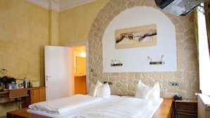 A double bed with white linens, a wooden bedside table, a stone wall, and a painting above the bed. - Hotel Deutsches Haus (Braunschweig)