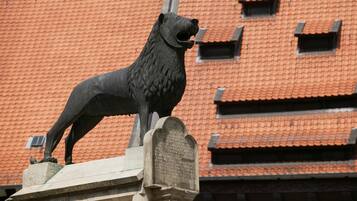 Une statue de lion, placée sur un piédestal et agrémentée d’une plaque commémorative, se dresse devant un bâtiment dont le toit est recouvert de tuiles rouges.