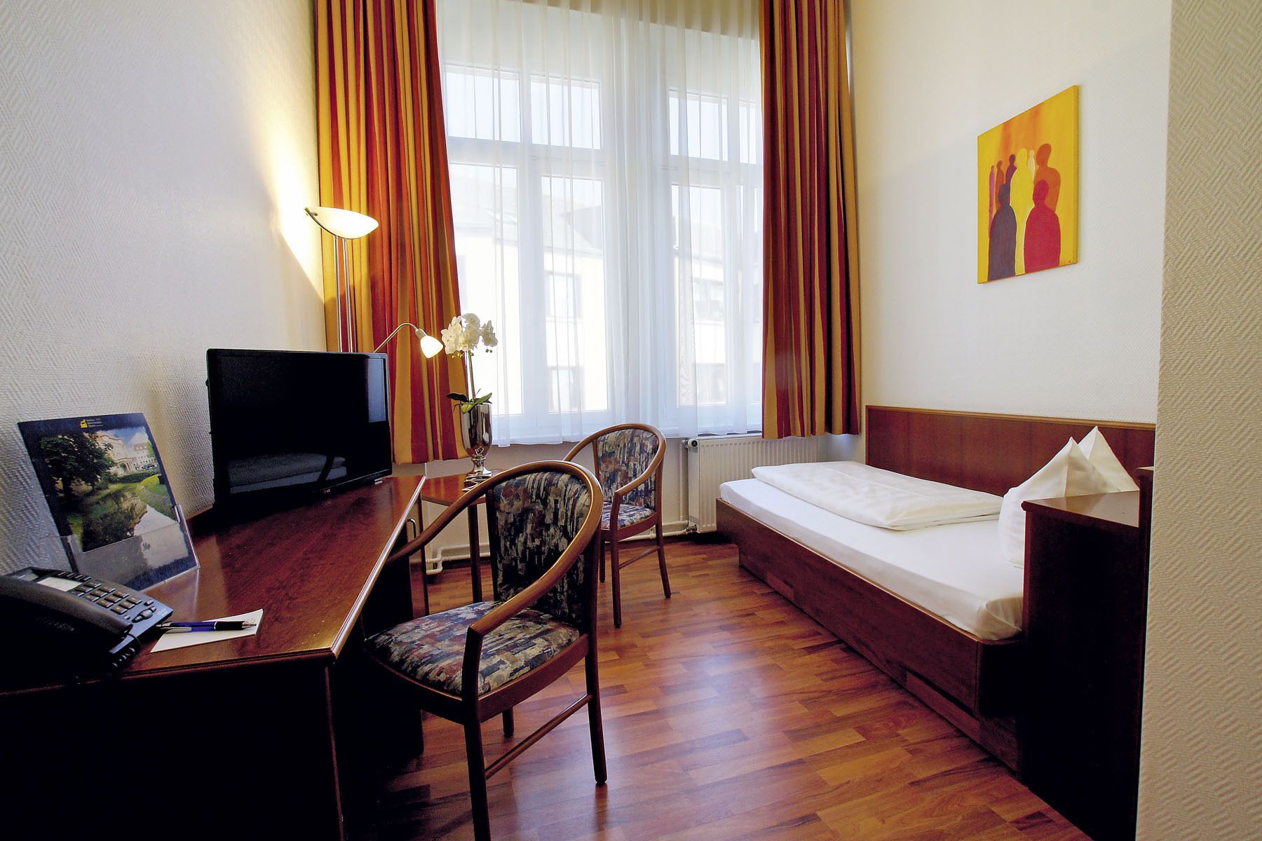 Een hotelkamer met een houten bureau, een televisie, een bed en een stoel.