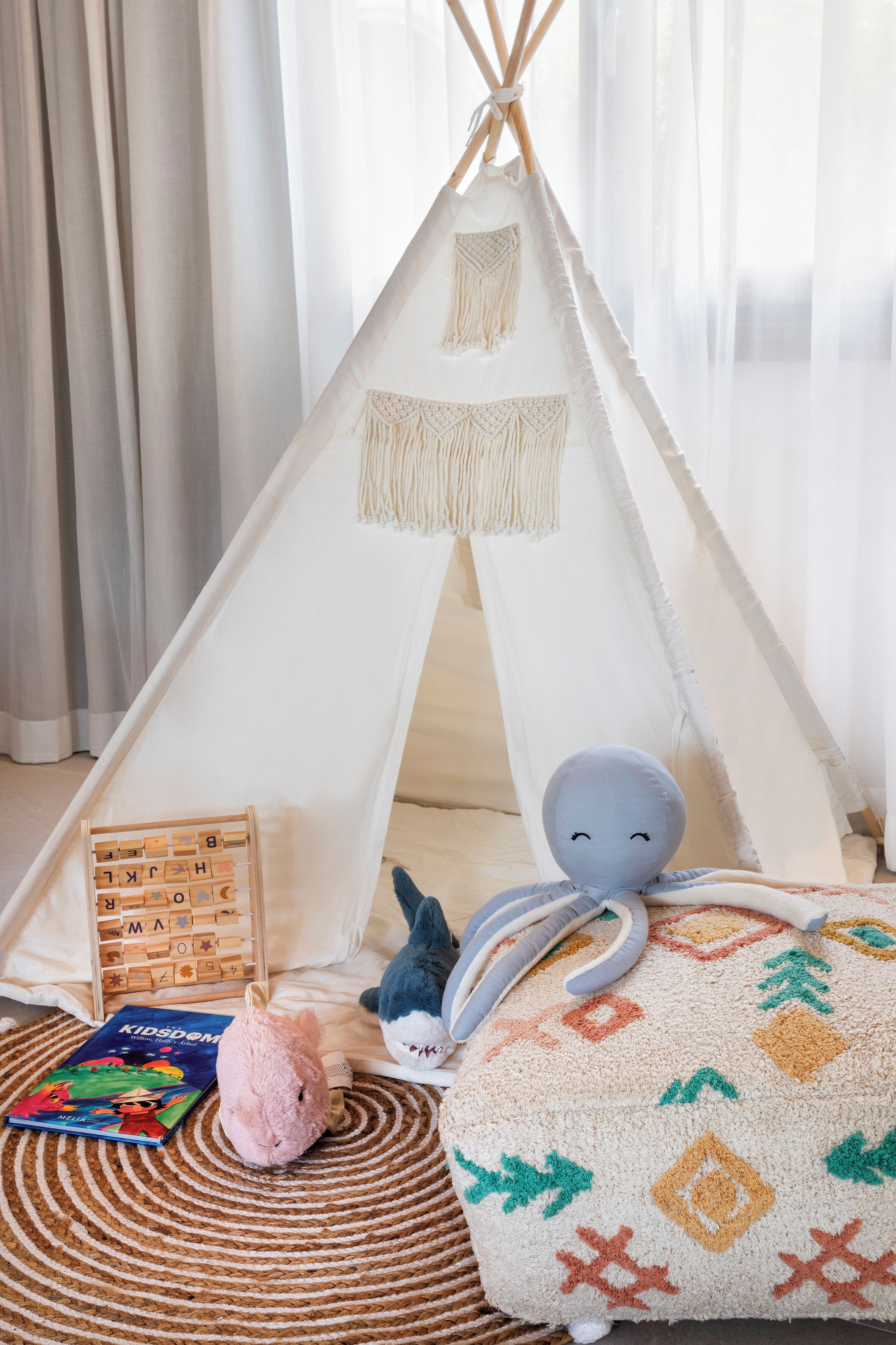 Un rincón infantil acogedor con una tienda tipi, un peluche de pulpo, un libro y un cojín estampado.