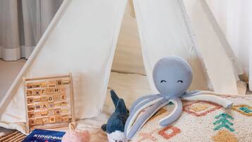 Un rincón infantil acogedor con una tienda tipi, un peluche de pulpo, un libro y un cojín estampado.