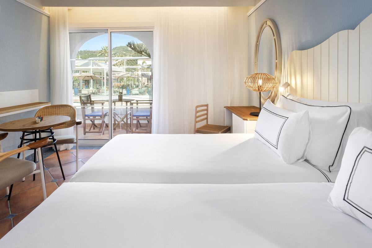 Ein Hotelzimmer mit einem großen Bett, einem Esstisch, Stühlen und Blick ins Freie.