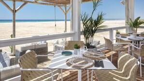 Un patio frente a la playa con mobiliario de mimbre, una mesa lista para comer y vistas a la playa.