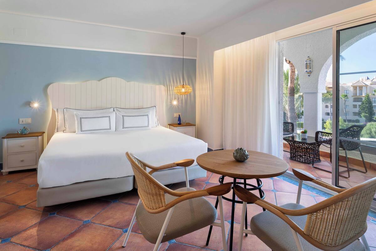 Ein Hotelzimmer mit einem großen Bett, einem runden Tisch mit Stühlen und einem Balkon mit Gartenmöbeln.
