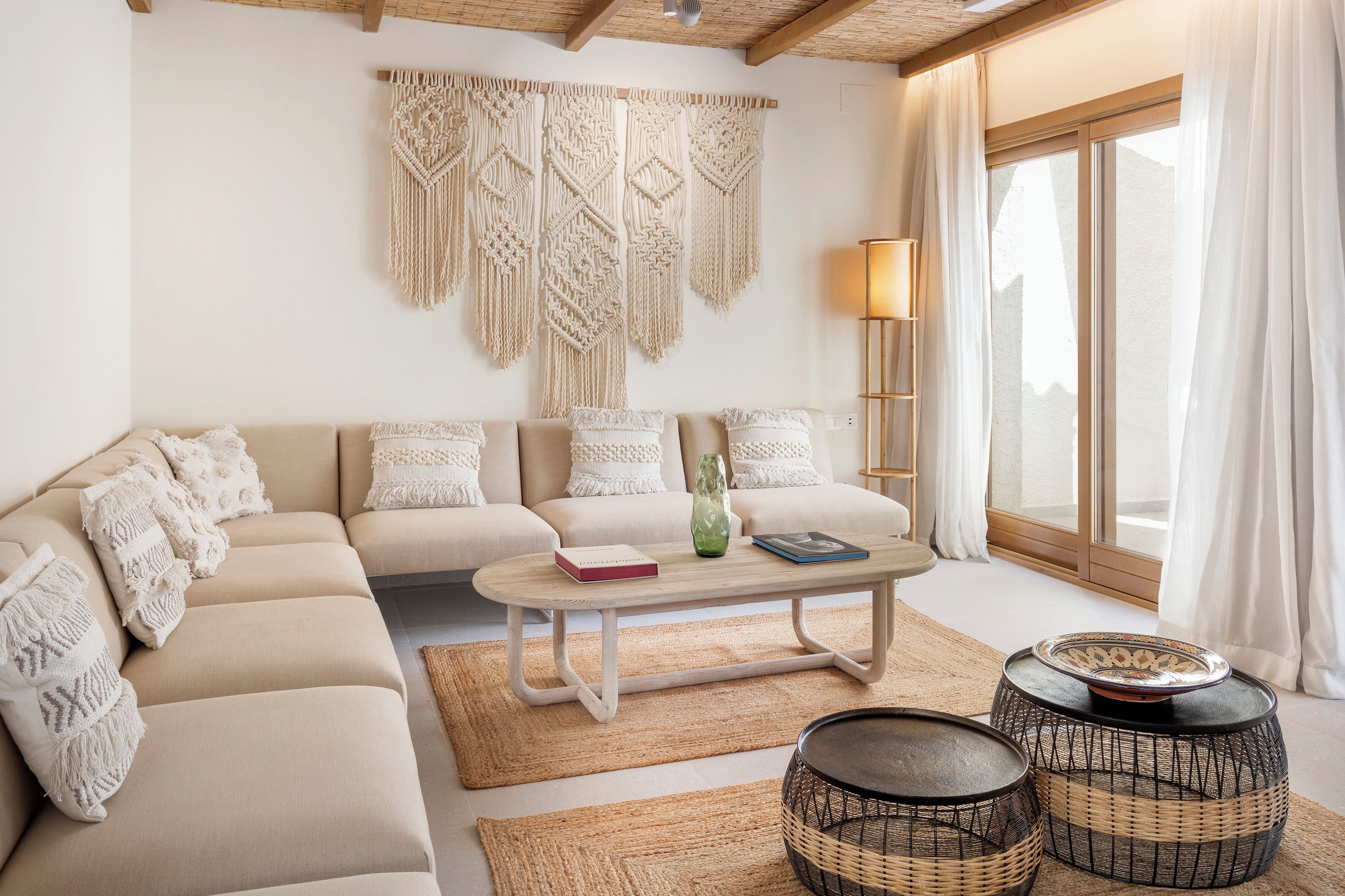 A modern living room with a beige sectional sofa, a wooden coffee table, and macramé wall hangings.