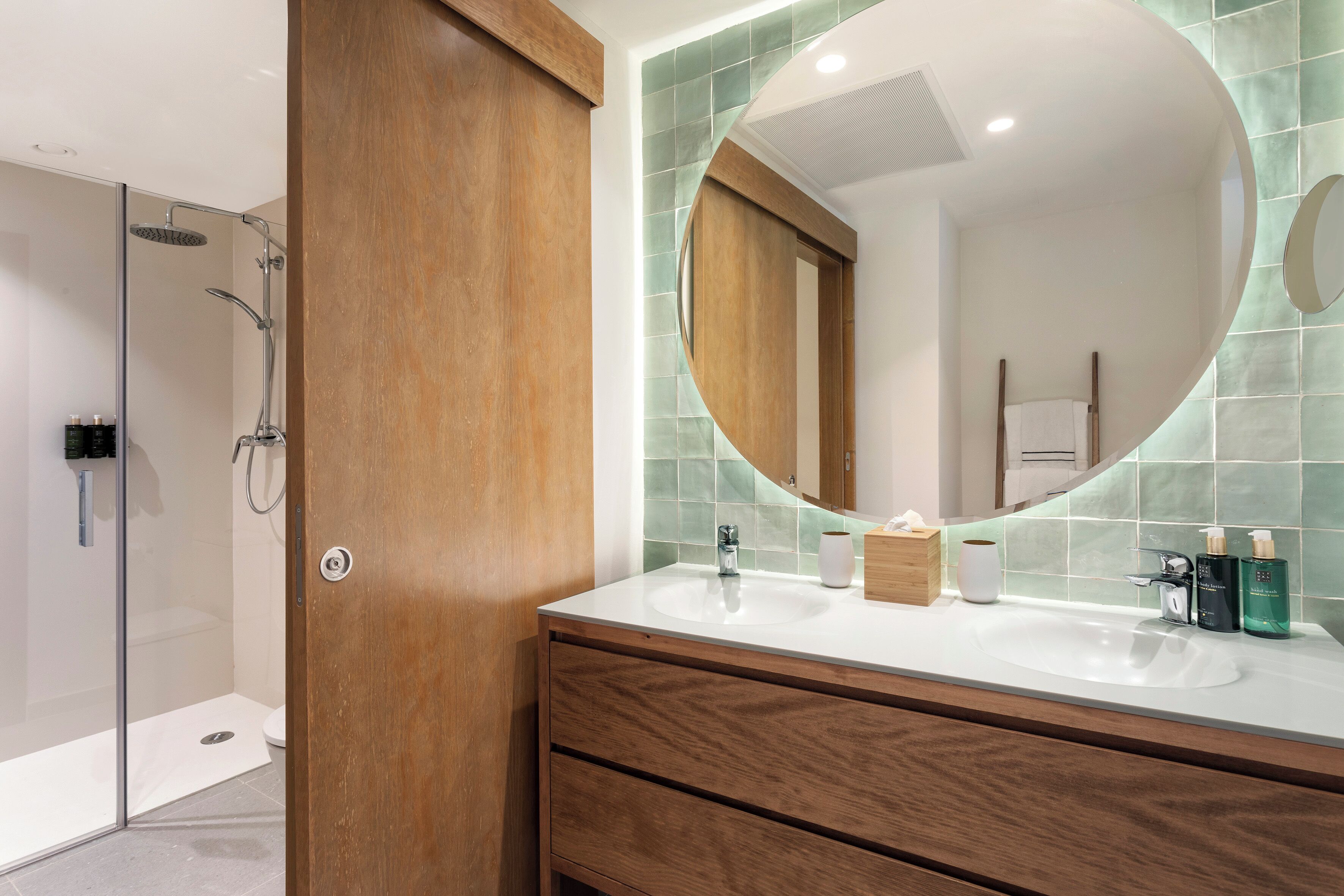 Un baño moderno con tocador de madera, un espejo grande y zona de ducha.