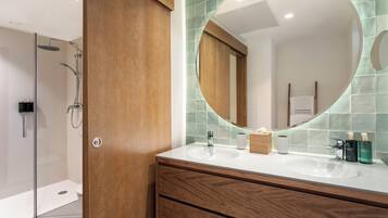 Un baño moderno con tocador de madera, un espejo grande y zona de ducha.