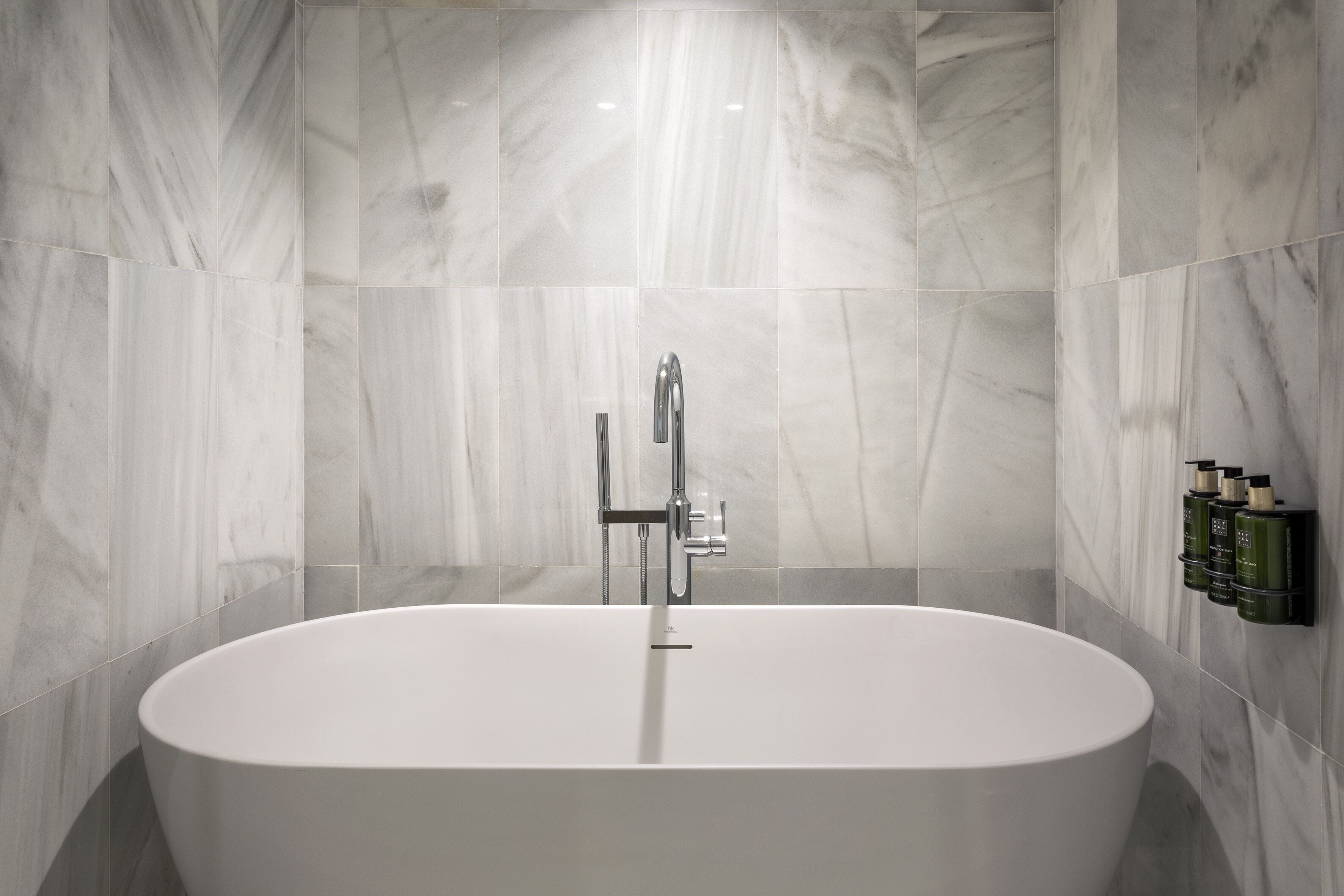 A modern bathroom with a freestanding bathtub, marble walls, and a wall-mounted showerhead.