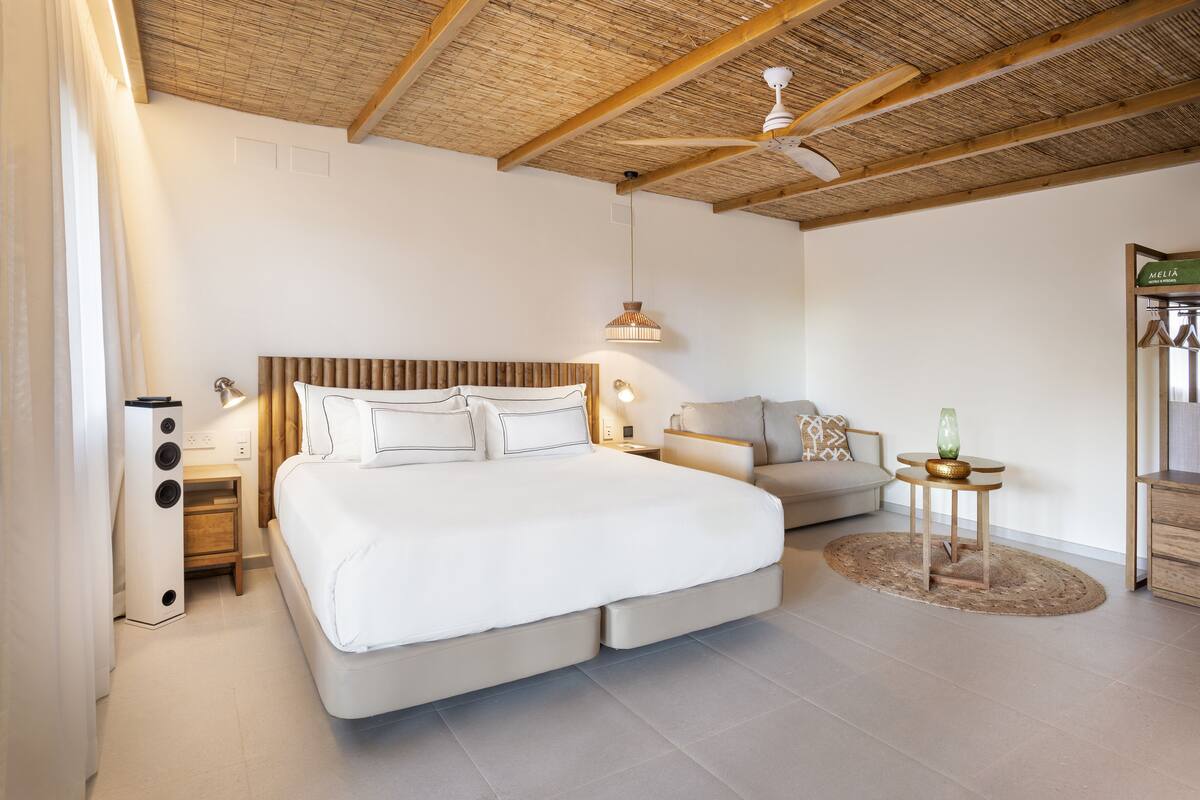 Ein geräumiges Schlafzimmer mit einem großen Bett, einer Couch, einem kleinen Tisch und einem Deckenventilator.