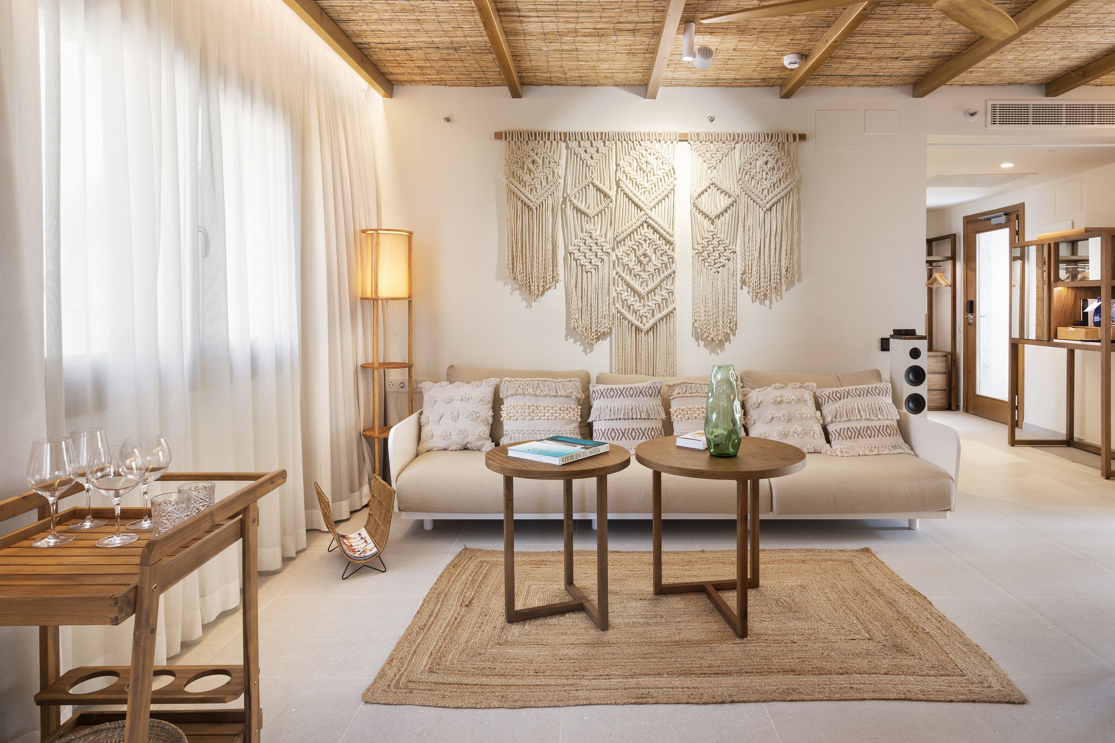 Un salon comprenant un canapé, deux tables rondes, un tapis tissé et une décoration murale en macramé.