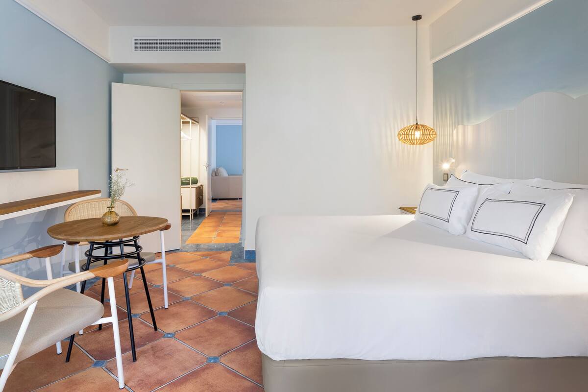 Ein Hotelzimmer mit einem Bett, einem an der Wand befestigten Fernseher, einem Esstisch mit Stühlen und einer Pendelleuchte.