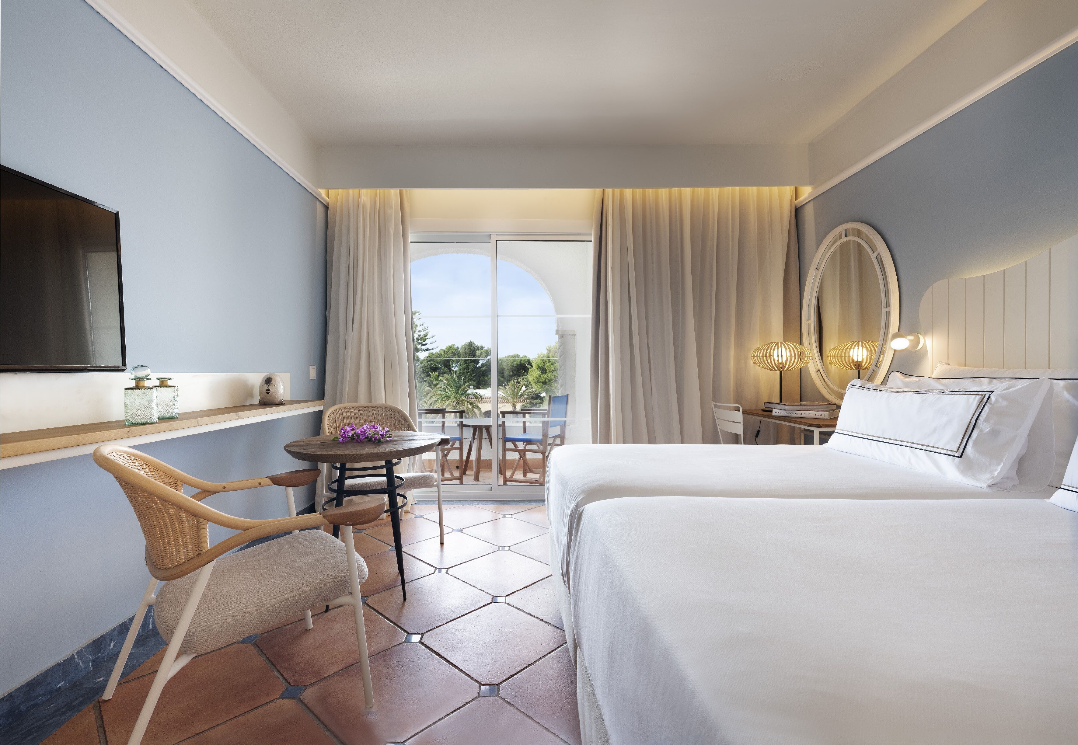 Ein Hotelzimmer mit Bett, Fernseher, einem kleinen Tisch mit Stühlen und einem Balkon mit Blick.