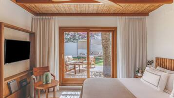 A bedroom with a bed, a TV, a chair, a small table, and a sliding glass door leading to an outdoor area with a table and chairs.