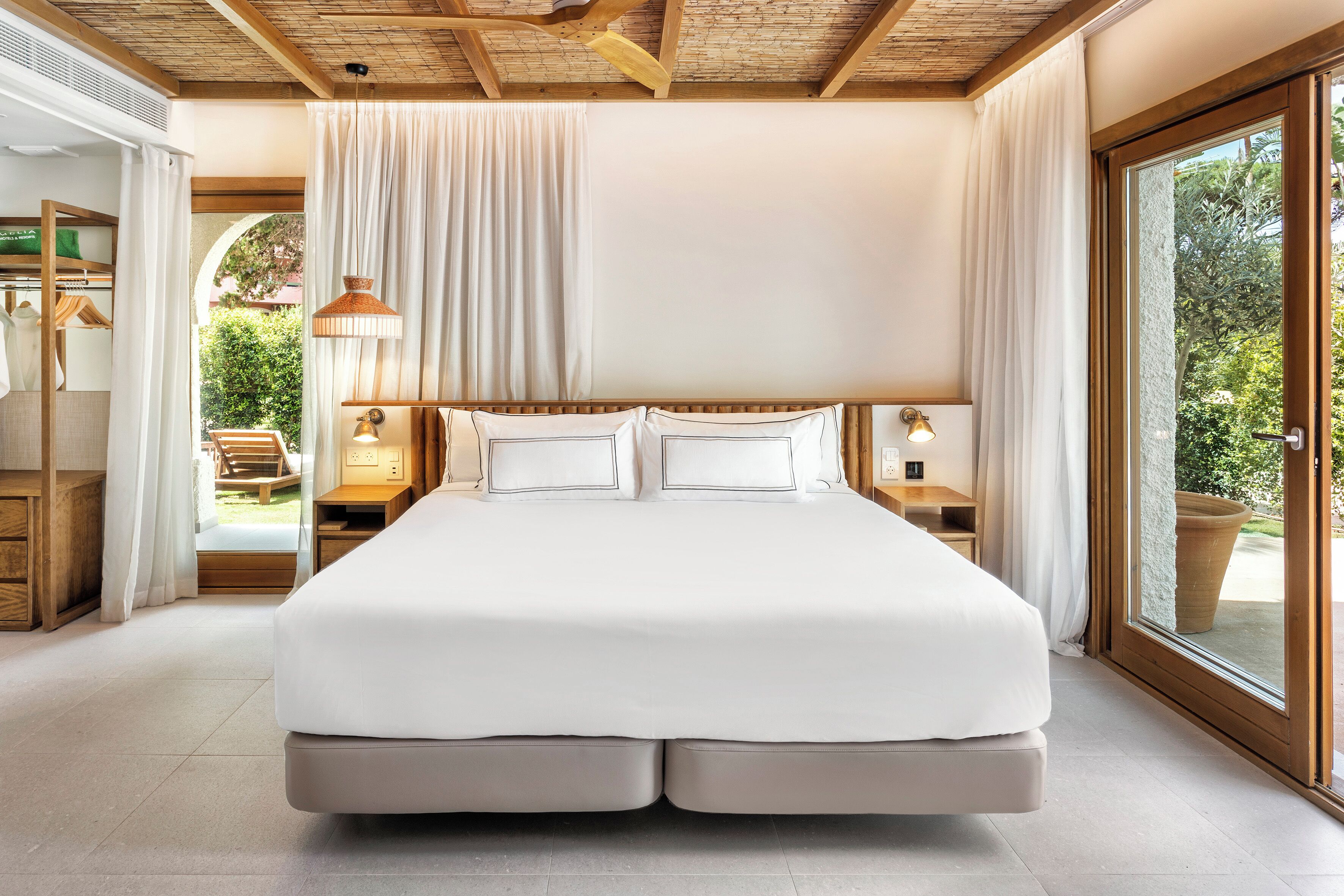 Ruime slaapkamer met een groot bed, houten balken in het plafond, uitzicht op groen en een schuifdeur naar buiten.