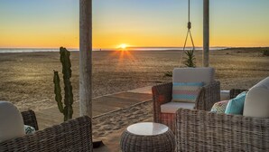 Un área de estar junto a la playa con mobiliario de mimbre y vista al atardecer sobre el océano.