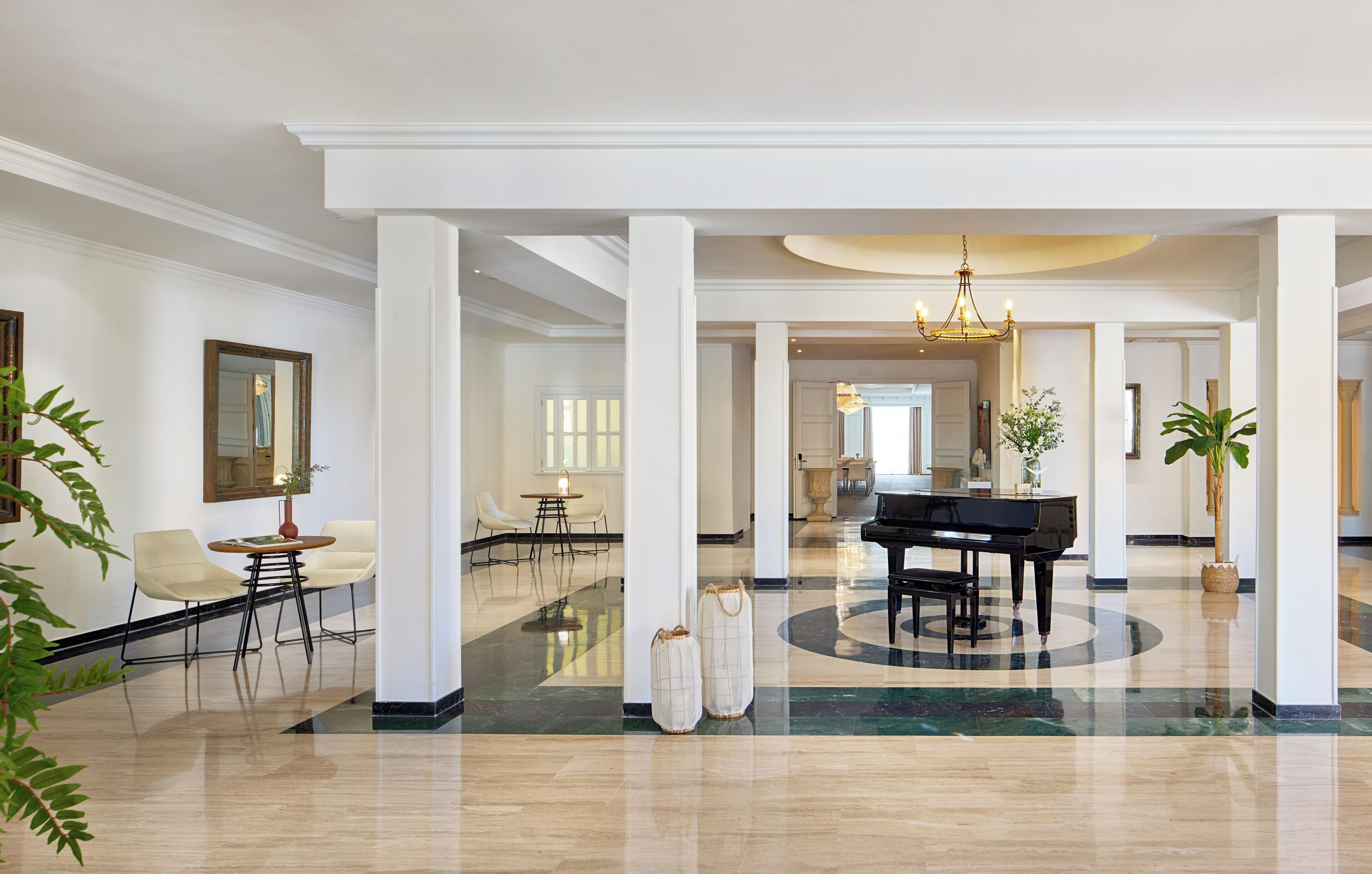 A spacious lobby with a grand piano, white columns, and a polished marble floor.